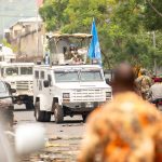 UN armored vehicles and peacekeepers patrol a busy urban street.