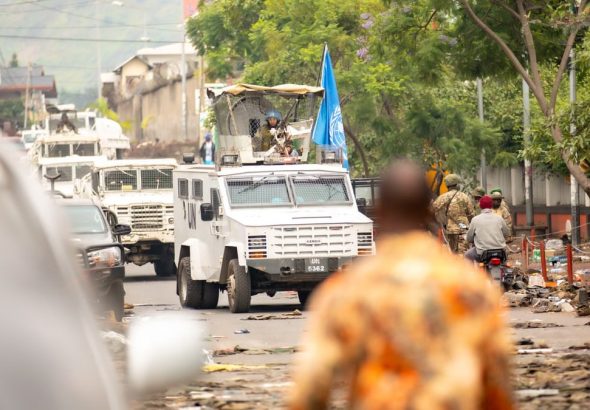 UN armored vehicles and peacekeepers patrol a busy urban street.