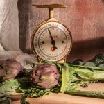 Artichokes and scale sit on a wooden table.