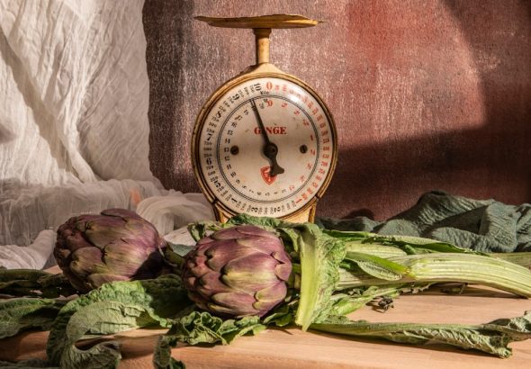 Artichokes and scale sit on a wooden table.
