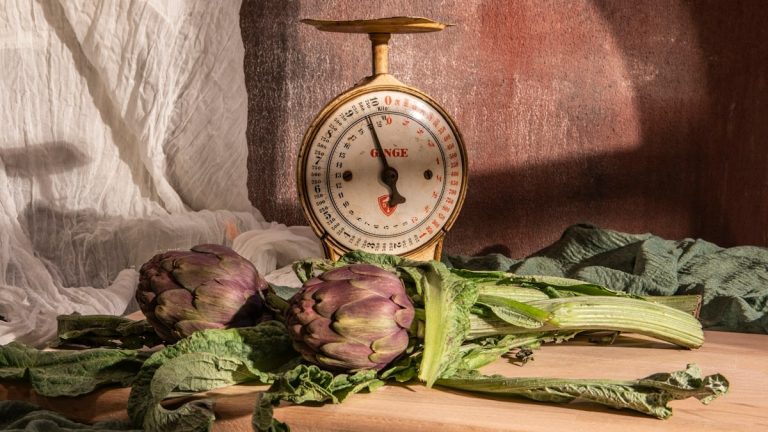 Artichokes and scale sit on a wooden table.