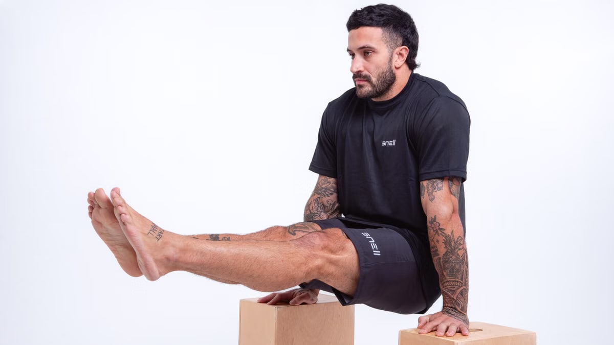 Man demonstrating strength in studio setting, wearing black sportswear and showcasing tattoos.